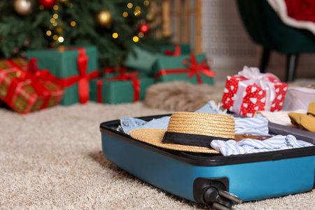 Suitcase with clothes and gift against blurred lights indoors, closeup with space for text. Christmas vacationの写真素材