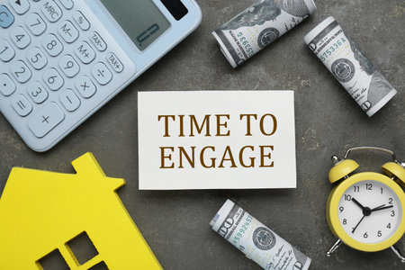 Card with text Time To Engage, alarm clock, dollars, calculator and house model on gray table. Flat layの写真素材