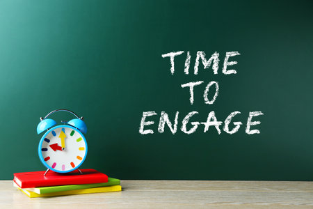 Time To Engage written on chalkboard. Alarm clock and books on wooden tableの写真素材