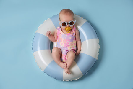 Cute little baby with sunglasses and pacifier on inflatable ring against light blue background, top viewの写真素材