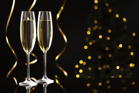 Merry Christmas and Happy New Year. Flute glasses with sparkling wine and serpentine streamers on black background against blurred lights. Space for textの写真素材