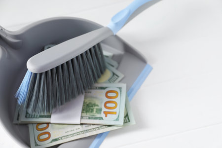 Dustpan with broom and dollar banknotes on white wooden surface, closeup. Space for textの写真素材