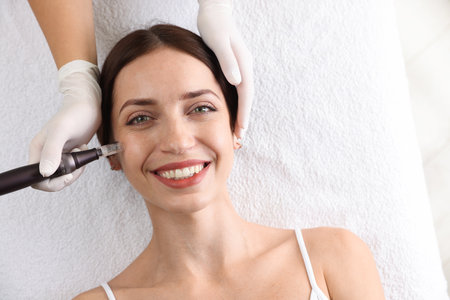 Woman undergoing microneedling procedure in beauty salon, top view