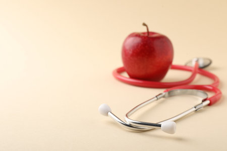 Ripe apple and stethoscope on beige background, selective focus. Space for textの写真素材