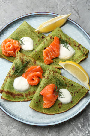 Tasty spinach crepes with salmon, sour cream, dill and lemon on gray table, top viewの写真素材
