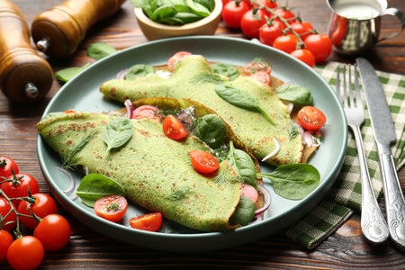 Tasty spinach crepes with tomatoes, onion, sour cream and leaves on wooden table, closeupの写真素材