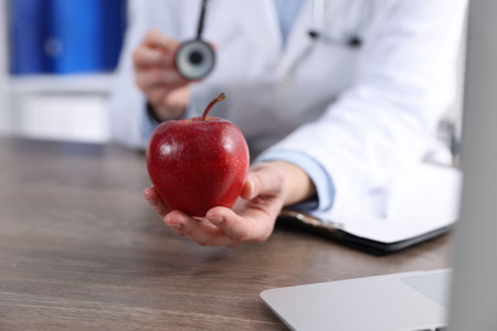 Doctor with ripe apple at wooden desk, closeupの写真素材