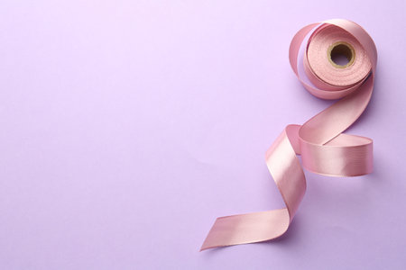 Roll of pink ribbon on violet background, top view. Space for textの写真素材