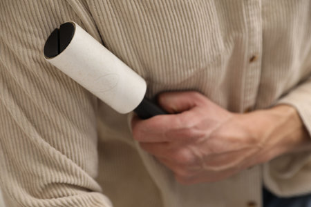 Man cleaning shirt with lint roller at home, closeupの写真素材