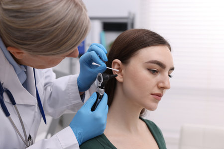 Hearing test. Doctor examining patient's ear with otoscope and cotton swab in clinicの写真素材