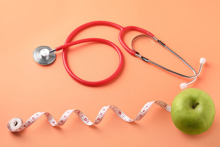Ripe apple, stethoscope and measuring tape on pale orange background, flat layの写真素材