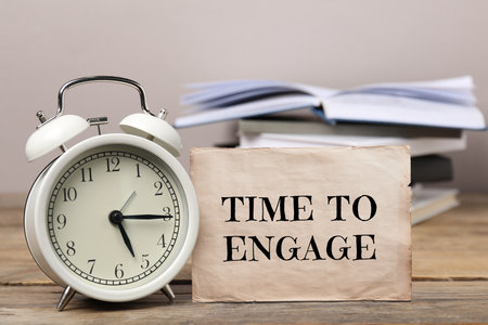 Card with text Time To Engage, alarm clock and notebooks on wooden tableの写真素材