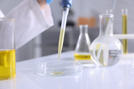 Scientist with dripping motor oil into Petri dish at table in laboratory, closeupの写真素材