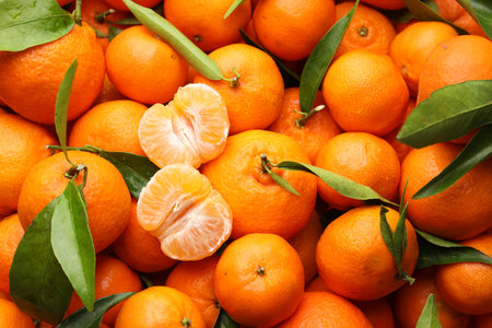 Many fresh ripe tangerines with green leaves as background, top viewの写真素材