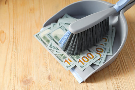 Dustpan with broom and dollar banknotes on wooden surface, closeup. Space for textの写真素材