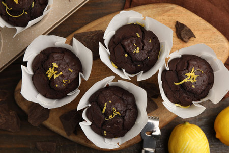 Tasty chocolate muffins with lemon zest and peeler on wooden table, flat layの写真素材