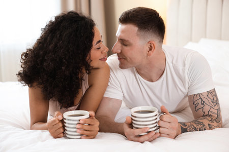 Lovely couple enjoying hot drinks in bed at homeの写真素材