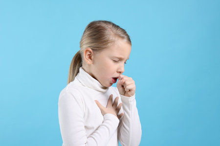 Little girl coughing on light blue background. Cold symptomの写真素材