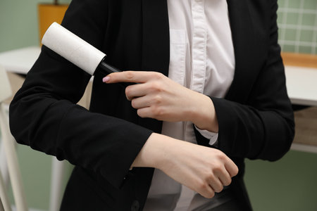 Woman cleaning jacket with lint roller in office, closeupの写真素材