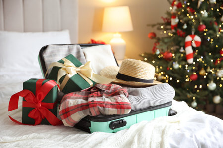 Suitcase with clothes and gifts on bed in festive decorated room. Christmas vacationの写真素材