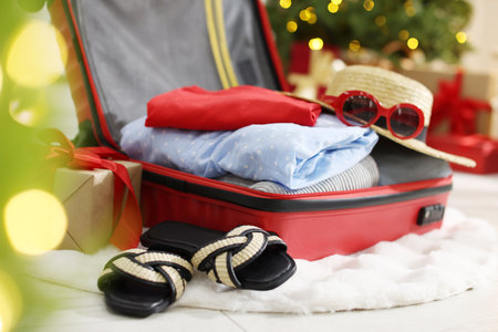 Suitcase with clothes, sunglasses, shoes and gifts on floor in festive decorated room, closeup. Christmas vacationの写真素材