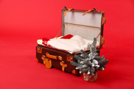 Suitcase with clothes and decorative fir tree on red background. Christmas vacationの写真素材