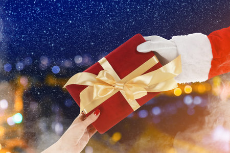 Santa Claus giving gift box to woman under falling snow outdoors, closeupの写真素材