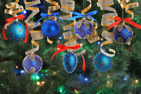 Beautiful Christmas ornaments and streamers hanging against blurred tree with festive lights. Winter holidays greeting cardの写真素材