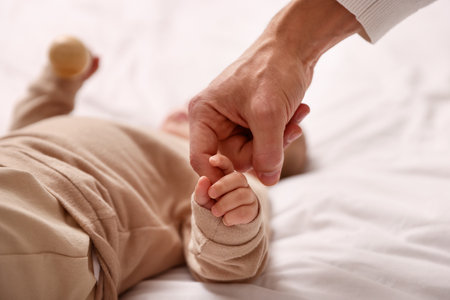 Cute baby holding father's finger on bed at home, closeupの写真素材