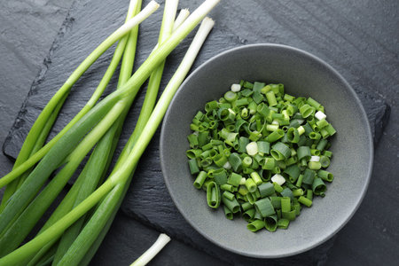 Whole and cut fresh green onions on black table, top view