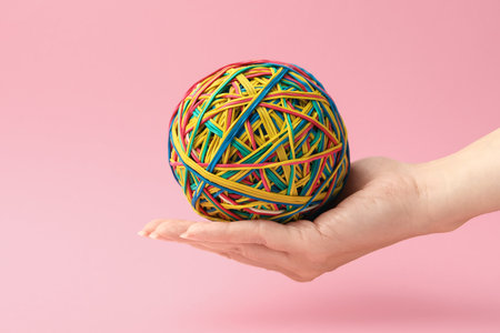 Woman with ball made of many colorful rubber bands on pink background, closeup