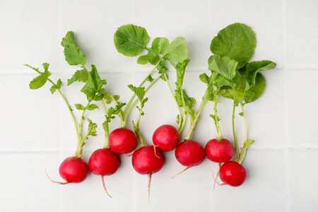 Fresh radishes with green leaves on white tiled table, flat layの写真素材