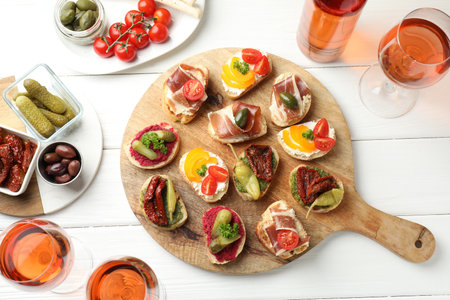 Tasty bruschettas with prosciutto and rose wine served on white wooden table, flat lay