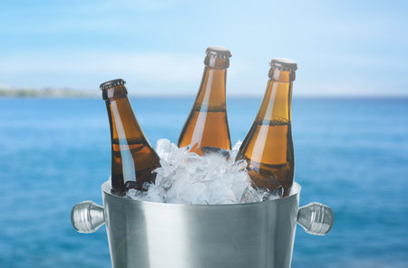 Beer in metal bucket with ice near sea. Refreshing summer drinkの写真素材
