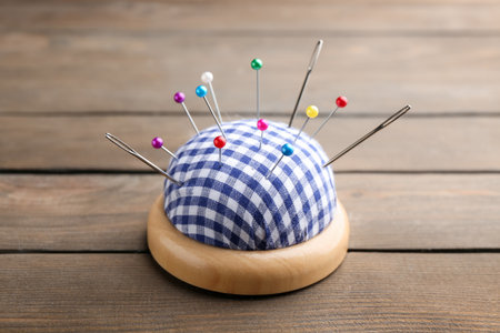 Checkered pincushion with pins and needles on wooden table, closeup