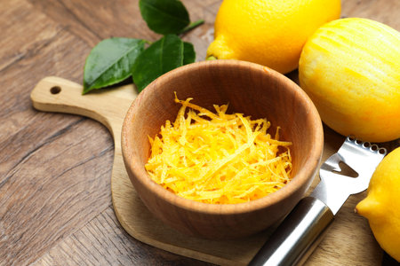 Lemon zest, fresh fruits and zester tool on wooden table, closeup