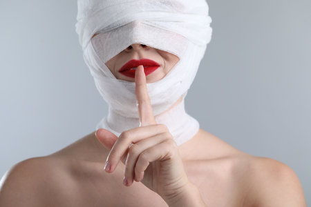 Woman with face wrapped in medical bandage after plastic surgery operation on light gray background, closeupの写真素材