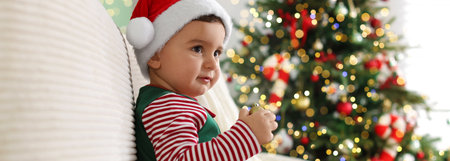 Little boy in Santa hat on sofa in room decorated for Christmas