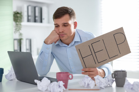 Man with laptop and sign Help at table in office