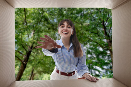 Woman looking into cardboard box against trees outdoors, view from inside package