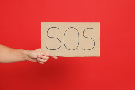 Man holding sign with word SOS on red background, closeupの写真素材