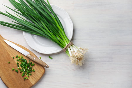 Fresh ripe green onions and knife on white wooden table, flat lay. Space for text