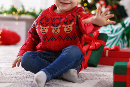 Cute little baby playing with toy car and Christmas gifts on floor in festive decorated room, closeupの写真素材