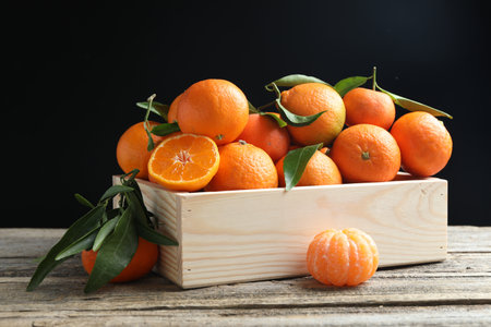 Fresh tangerines and green leaves in crate on wooden table against black background, closeupの写真素材
