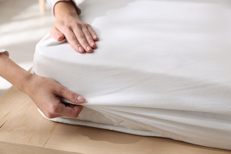 Woman putting bed sheet on mattress indoors, closeupの写真素材