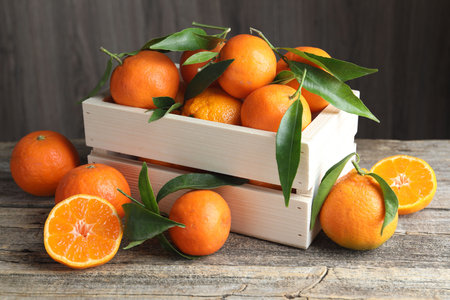 Fresh tangerines and green leaves in crate on wooden table, closeupの写真素材