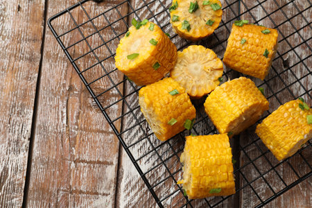 Pieces of boiled corn cobs with green onion on wooden table, top view. Space for text