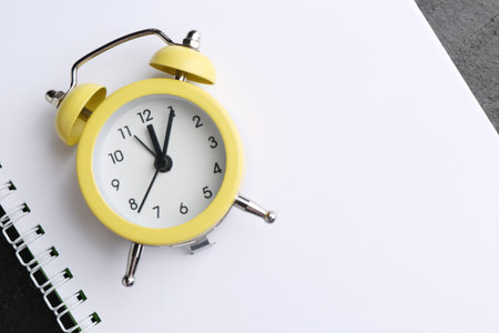 Alarm clock and notebook on black table, top view