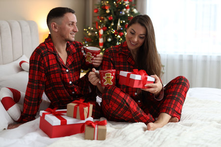 Happy couple in pajamas with Christmas gifts on bed at homeの写真素材