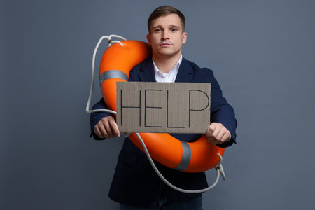 Man with life ring holding cardboard sign Help on gray backgroundの写真素材